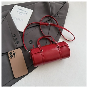 Flat lay of a red cylindrical PU leather handbag with silver hardware and shoulder strap