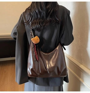 Detail view of large dark brown leather shoulder bag with bear charm on a model's back