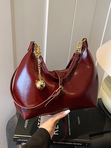 Borsa hobo rosso scuro lucida con dettagli dorati su un libro, stile minimalista