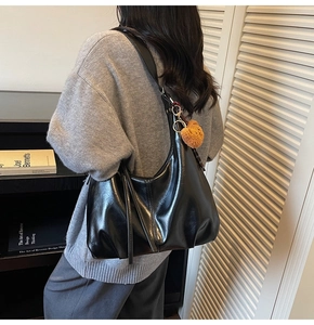 Close-up of black glossy shoulder bag with a brown teddy bear charm and wide strap
