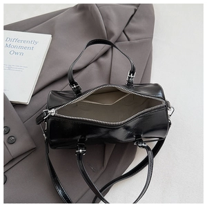 Detail of glossy black cylinder bag with dual zippers and woven interior lining