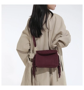 Detail of burgundy suede shoulder bag with fringe tassels and woven edge on beige coat