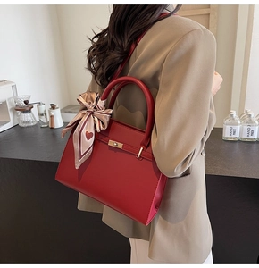 Détail d'un sac à main rouge avec fermoir doré et foulard en soie dans un décor de café
