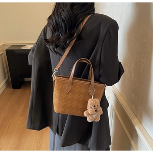 Detail of brown suede bucket bag featuring embossed patterns and a cute plush bear charm