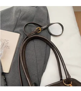 Close-up of dark brown leather tote with smooth handles and adjustable gold buckle strap