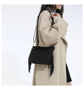 Side view of black suede crossbody bag with long side tassels and slim strap
