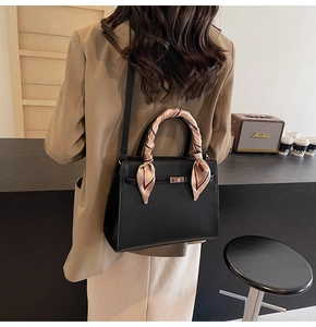 Détail d'un sac à main noir structuré avec foulard en soie et fermoir doré chic