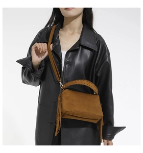 Detail shot of brown suede shoulder bag with woven handle and fringe tassel accent