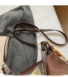 Close-up of brown suede shoulder bag with gold hardware and colorful beaded keychain