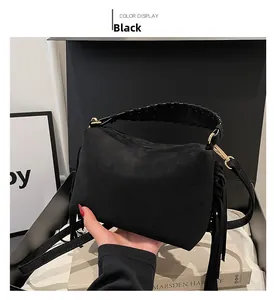 Detail of black suede shoulder bag featuring tassel accents and woven handle straps