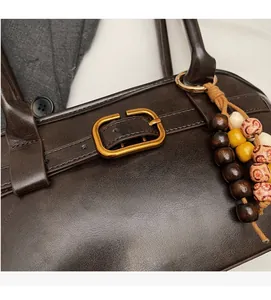Macro detail of dark brown leather shoulder bag with vintage gold buckle and beaded charm
