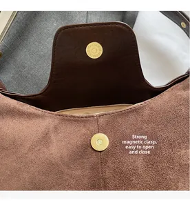 Macro detail of golden magnetic buckle on brown suede bag with neat stitching