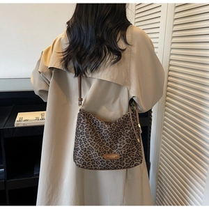 Détail d'un sac bandoulière léopard avec plaque métallique et fine lanière en cuir