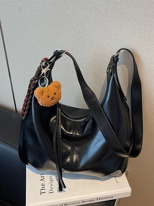 Chic black oily leather hobo bag with teddy bear charm on a stack of art books
