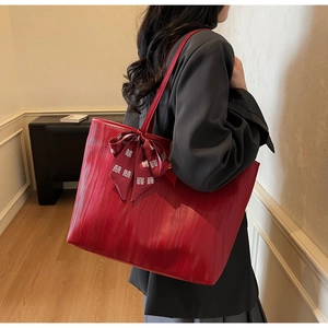 Detail of red leather tote bag featuring a decorative festive bow with traditional motifs