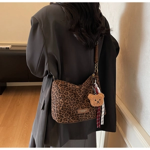 Détail d'un sac cabas léopard avec pendentif ours en peluche porté sur un blazer gris