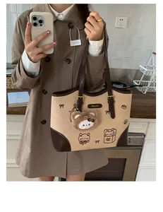 Dettaglio della borsa tote beige con stampe di gatti e portachiavi a forma di orsetto