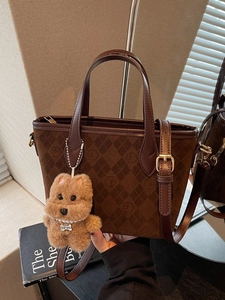 Brown suede bucket bag with diamond quilting and plush dog charm on a mirrored surface