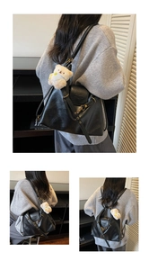 Detail of black faux leather tote bag with gold buckle and white bear plush charm