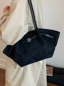 Large black matte tote bag with silver buckle worn by a model in a beige trench coat