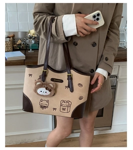 Dettaglio di una borsa tote beige con ricamo a gatto e ciondolo orsetto di peluche