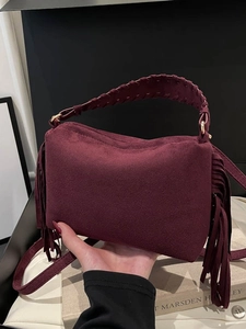 Burgundy suede shoulder bag with fringe details and woven handle shown from the side
