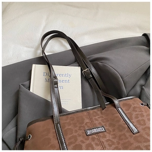Detail of leopard print tote bag with brown leather strap and metal logo plaque