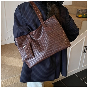Détail d'un grand sac cabas tressé marron foncé porté avec un blazer bleu marine