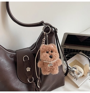 Detail of plush puppy bag charm with pearl necklace and engraved bone tag on tote bag