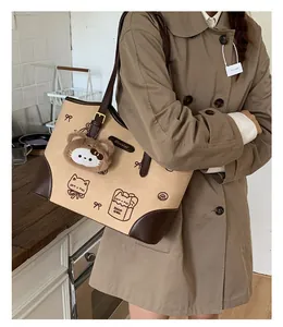 Dettaglio laterale di una grande borsa tote beige e marrone con ciondolo a forma di gatto
