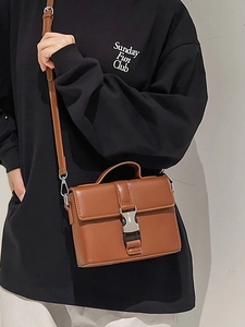 Deep brown leather small square bag with metal clasp and adjustable strap worn by a model