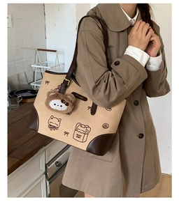 Dettaglio borsa tote in tela con stampe di gatti, finiture in pelle e ciondolo di peluche