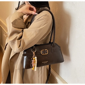 Detail of dark brown faux leather shoulder bag with gold logo and wooden beaded charm