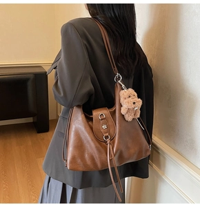 Detail of vintage brown leather tote bag with tassel decor and plush bear charm pendant