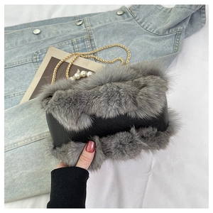 Detail of black pebbled leather handbag with gray faux fur trim and pearl gold chain