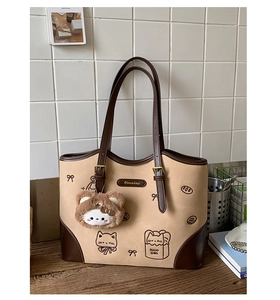 Dettaglio di una borsa tote beige con stampa di gatto, logo e ciondolo orsetto di peluche