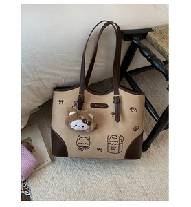 Dettaglio della borsa tote beige con stampe di gatti e ciondolo a testa di orsetto