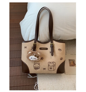 Dettaglio di una borsa tote patchwork chic con motivi a cartoni e ciondolo a orsetto