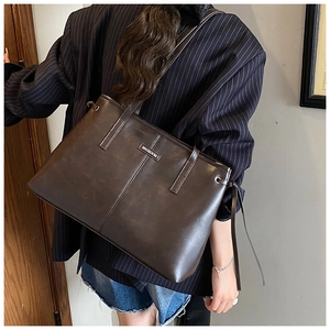Detail of dark brown leather tote bag with silver logo plaque and vertical stitching