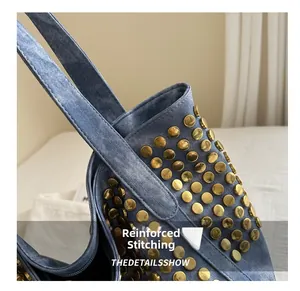 Détail de couture renforcée et clous dorés sur la bandoulière d'un sac cabas en jean