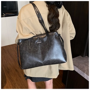 Close-up of charcoal gray faux leather tote bag showing vertical stitching and metal logo