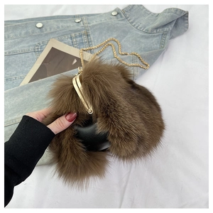 Detail of fox fur crossbody bag with gold chain strap and metal clasp on denim background