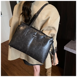 Close-up of black faux leather tote bag showing large capacity and metallic brand logo