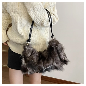Detail of grey plush faux fur shoulder bag with slender black strap on white knit sweater