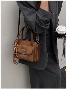 Detail of a brown suede bowling bag featuring a silver twist-lock pocket and woven tassel