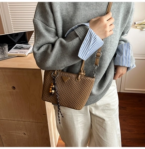 Detail of a brown quilted bucket bag with a metal triangle logo and woven beaded charm