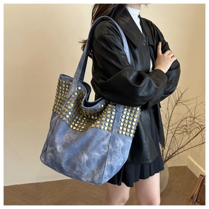 Détail du sac cabas en jean bleu avec clous dorés porté sur une veste en cuir