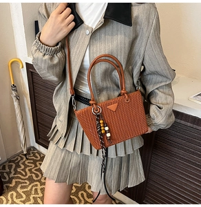Detail of a brown quilted bucket bag with a metal triangle logo and beaded charm detail