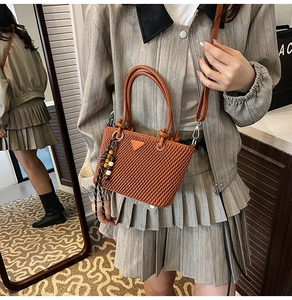 Detail of brown pleated bucket bag with dual handles and beaded charm accessory