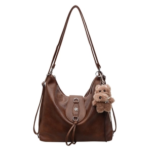 Brown large faux leather tote bag with floral buckle and plush dog charm on white background